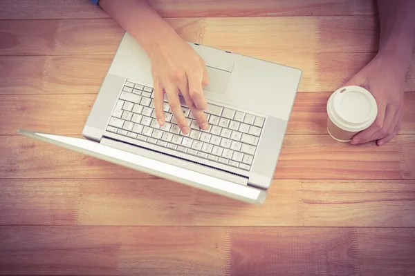 Homem segurando copo descartável enquanto digita no laptop — Fotografia de Stock