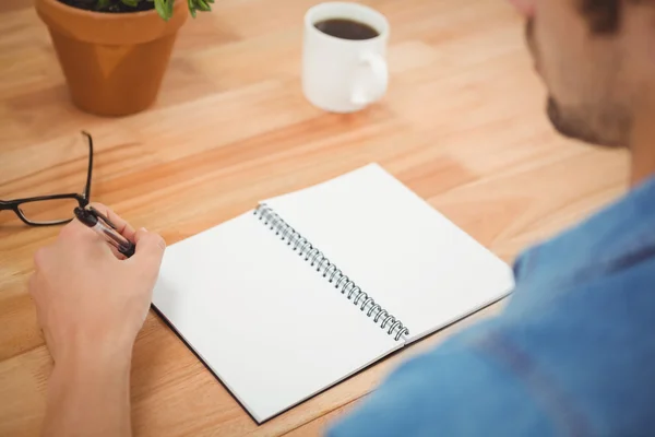 Hipster holding pen with spiral book and coffee on table — Stock Photo, Image