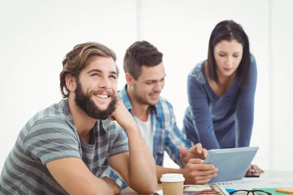 Sorrindo homem olhando para longe com colegas de trabalho usando tablet digital — Fotografia de Stock