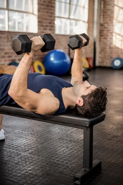 Man lifting dumbbells lying on exercise bench — Stock Photo, Image