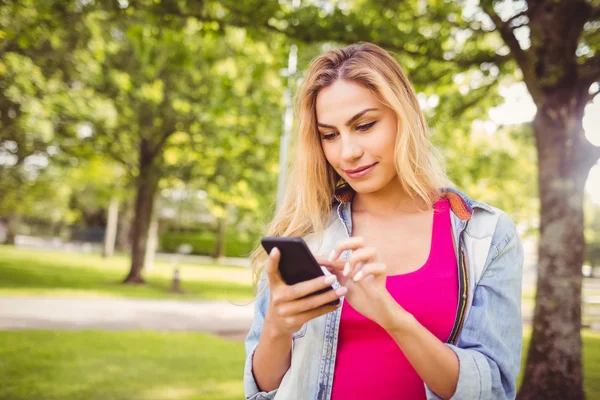 Uśmiechnięta kobieta korzystająca ze smartfona w parku — Zdjęcie stockowe