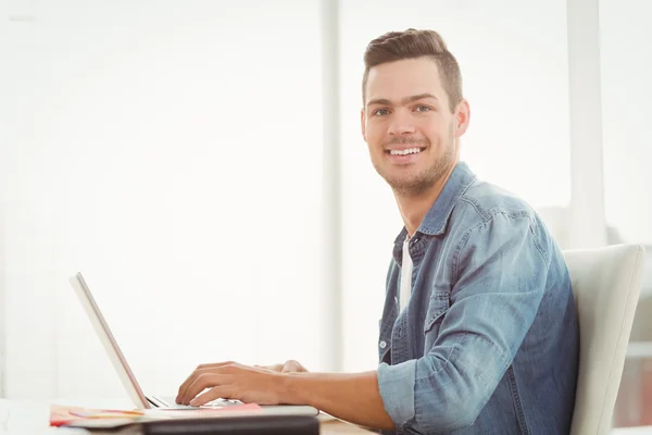 Portret van lachende jonge man die op laptop werkt — Stockfoto