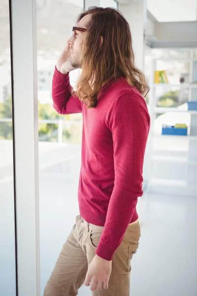 Hipster hablando en el teléfono móvil mientras está de pie por la ventana —  Fotos de Stock