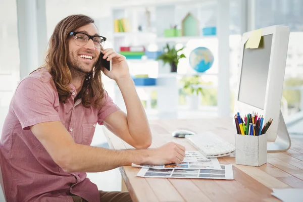 Happy hipster using mobile phone at computer desk — Stock Photo, Image
