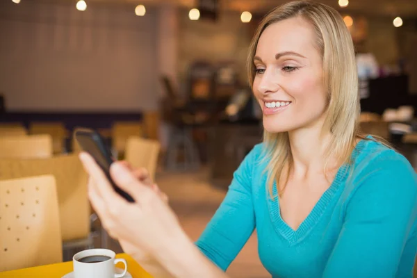 Junge Frau lächelt, während sie ihr Handy benutzt — Stockfoto