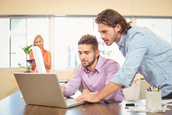 Businessmen working on laptop with female colleague in backgroun — Stock Photo, Image