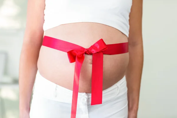 Buik van vrouw met rood lint — Stockfoto