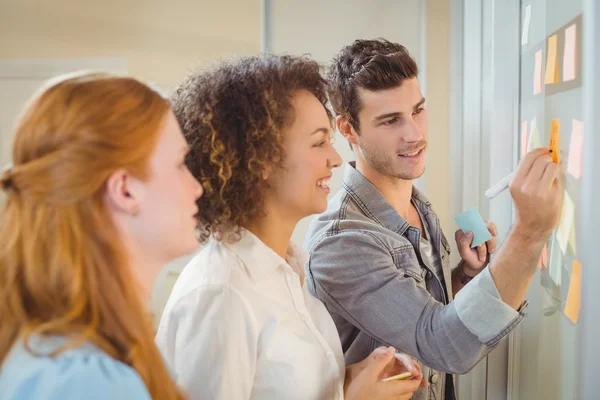 Empresario escribiendo en la pared de vidrio como colegas mujeres —  Fotos de Stock