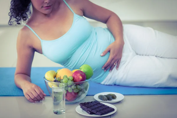 Mulher grávida deitada por frutas e chocolates — Fotografia de Stock