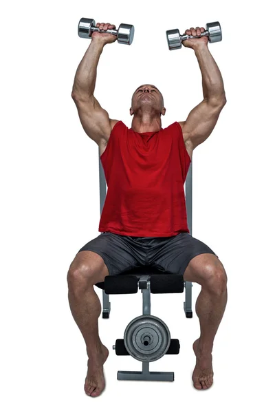 Healthy man lifting dumbbells while sitting on bench press Stock Image