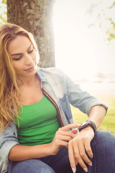 Woman touching smart watch while sitting under tree — Stock Photo, Image