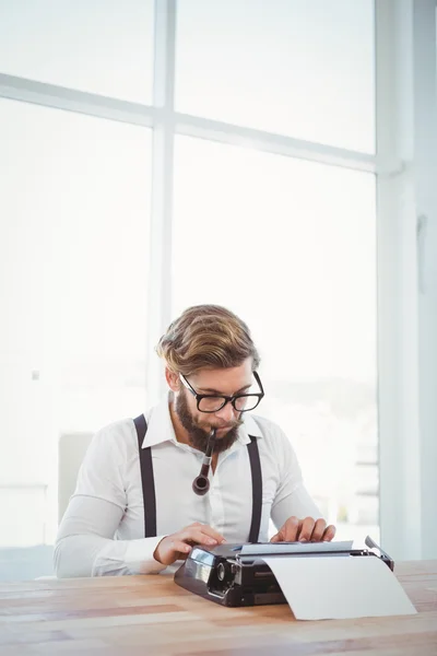 Hipster tupakointi putki työskennellessään kirjoituskoneen — kuvapankkivalokuva