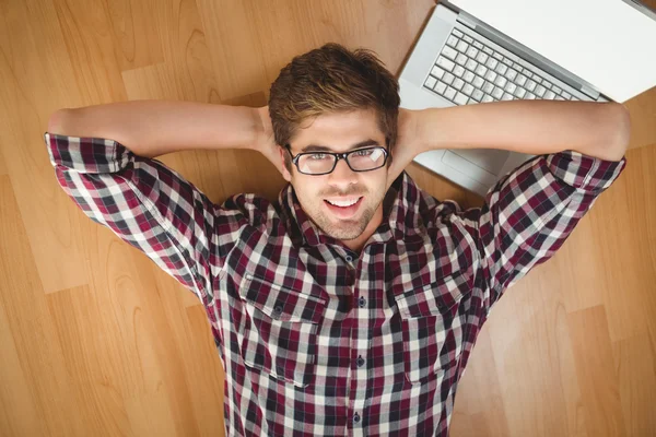 Empresário sorrindo enquanto deitado por laptop no chão de madeira — Fotografia de Stock