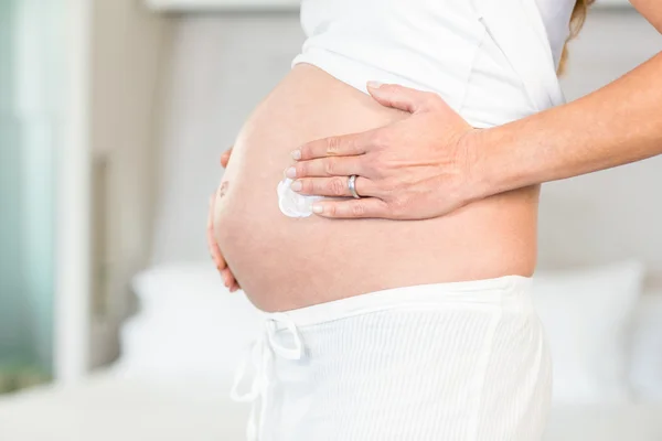 Sección media de la mujer que aplica crema en el vientre — Foto de Stock