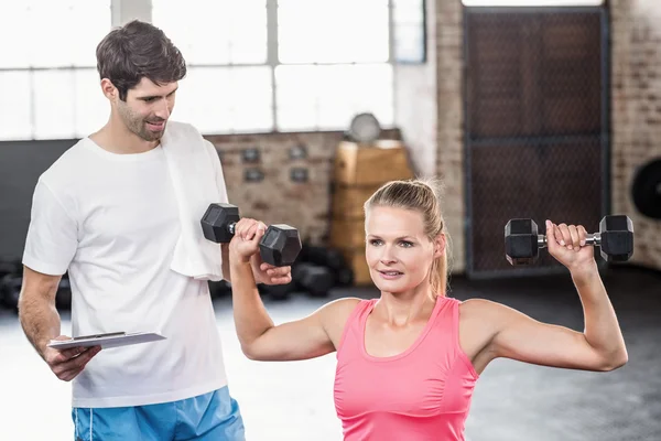 Fit woman lifting dumbbells with trainer — Stock Photo, Image