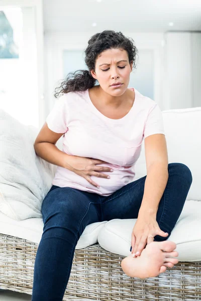 Pregnant woman touching feet while holding belly — Stock Photo, Image