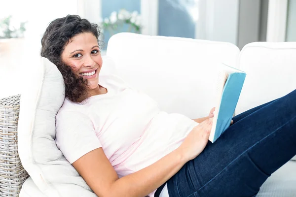 Mulher grávida feliz com livro no sofá — Fotografia de Stock