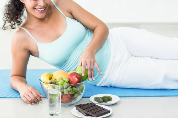 Lachende zwangere vrouw liggen door vruchten en chocolade — Stockfoto