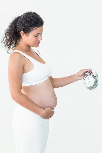 Zwangere vrouw wekker kijken terwijl het aanraken van de buik — Stockfoto