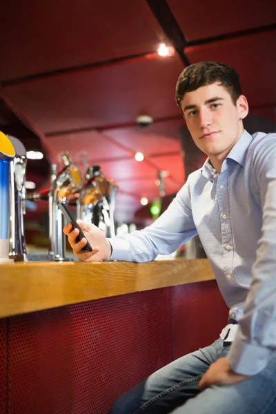 Confident man holding mobile phone at bar counter — Stock Photo, Image