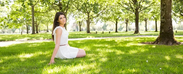 Młoda kobieta siedząca na użytki zielone w parku — Zdjęcie stockowe
