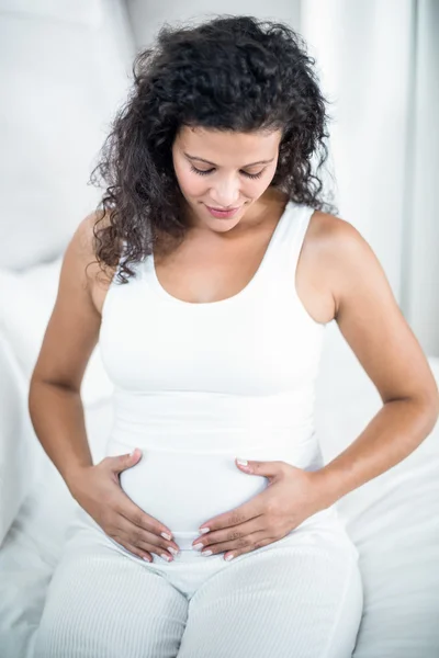 Mujer tocando su barriga mientras está sentada en la cama —  Fotos de Stock