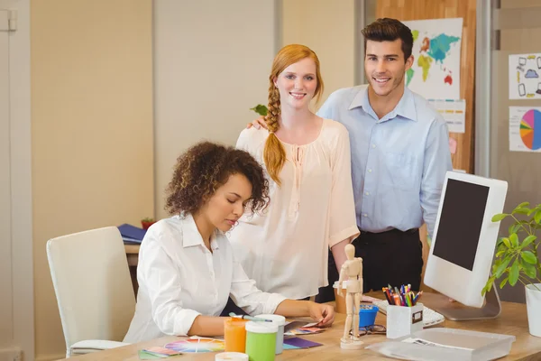 Business people standing by colleague working at desk — Stock Photo, Image