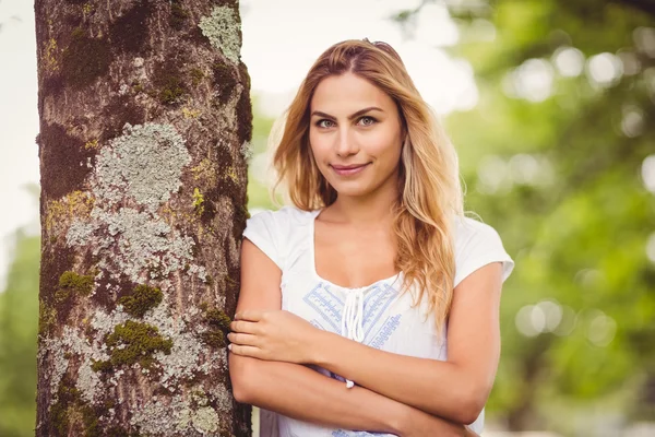 Leende kvinna med armar korsas stående av träd — Stockfoto