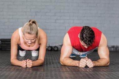 Fit smiling couple planking together in gym clipart