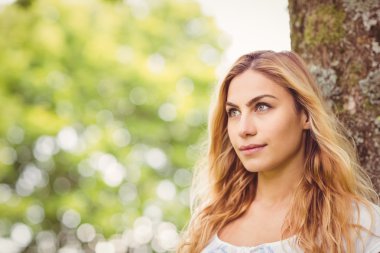 Beautiful woman looking away while standing by tree clipart