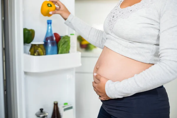 Mulher grávida segurando barriga pimenta da geladeira — Fotografia de Stock