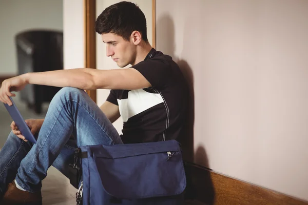 Male student with digital tablet sitting by wall in college — Stock Photo, Image