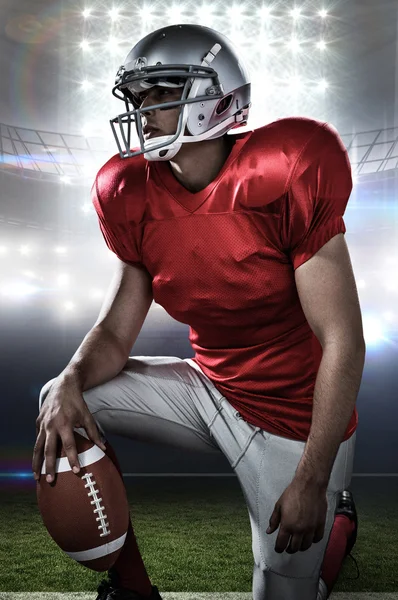 Composite image of sportsman holding american football while kne — Stock Photo, Image