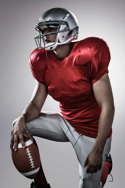 Спортсмен держит американский футбол на коленях — стоковое фото