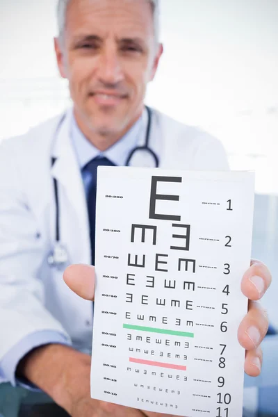 Médico masculino mostrando una hoja de prescripción en blanco contra la prueba ocular — Foto de Stock