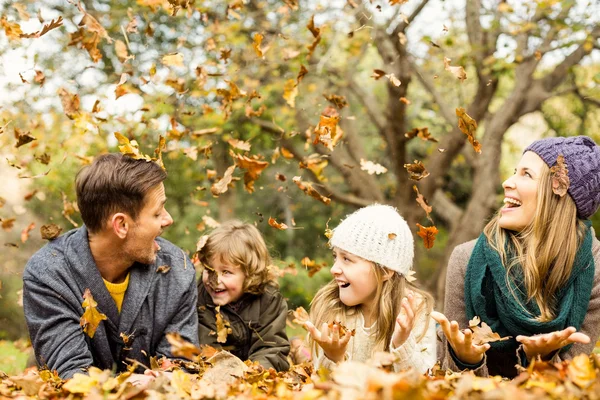 Lächelnde junge Familie wirft Blätter um sich — Stockfoto