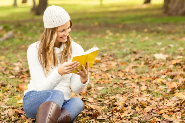 Sorrindo mulher bonita lendo um livro em folhas — Fotografia de Stock