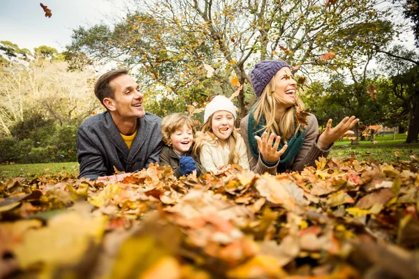 Smiling young family throwing leaves around — Stock Photo, Image