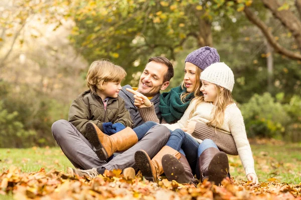 Uśmiechnięta młoda rodzina siedzący liście — Zdjęcie stockowe