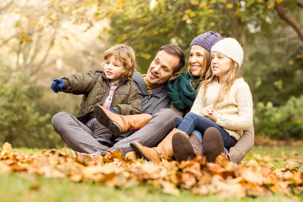 Sorridente giovane famiglia seduta in foglie — Foto Stock