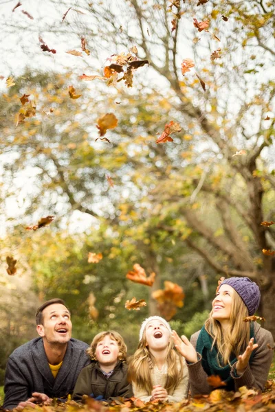 Улыбающаяся молодая семья разбрасывается листьями — стоковое фото
