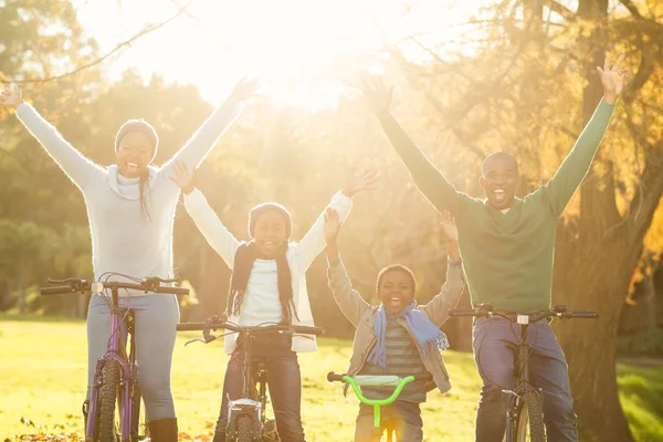 Joven familia sonriente haciendo un paseo en bicicleta con los brazos levantados —  Fotos de Stock