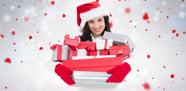 Imagen compuesta de morena sonriente en sombrero de santa celebración pila de regalos —  Fotos de Stock