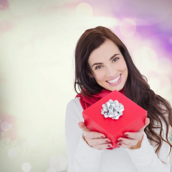 Happy brunette showing red gift with a bow — Stock Photo, Image