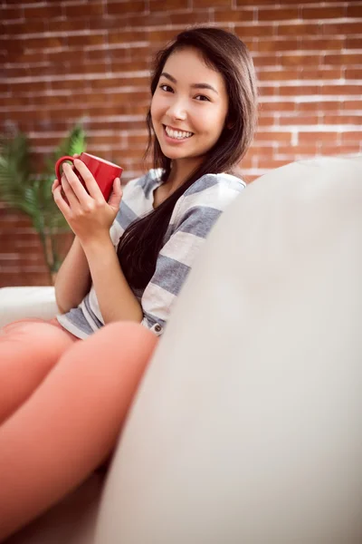 Sonriendo asiático mujer en sofá teniendo Caliente bebida —  Fotos de Stock