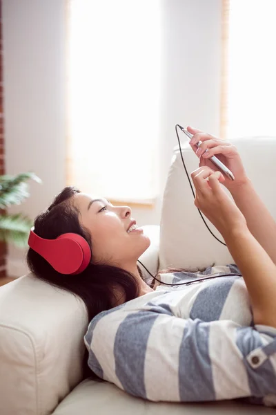 Sorrindo mulher asiática no sofá ouvindo música — Fotografia de Stock