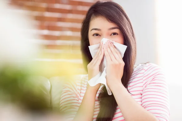 Asian woman blowing her nose on couch — Stock Photo, Image