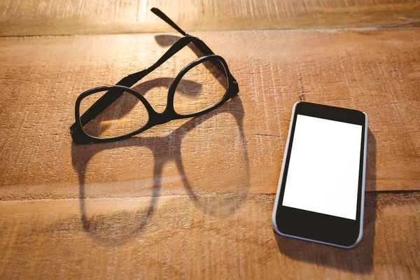 Smartphone en bril op houten plank — Stockfoto