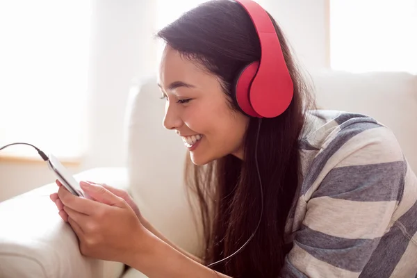 Sorridente donna asiatica sul divano ad ascoltare musica — Foto Stock