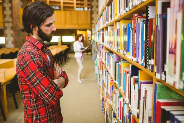 Hipster student plukken van een boek in de bibliotheek — Stockfoto